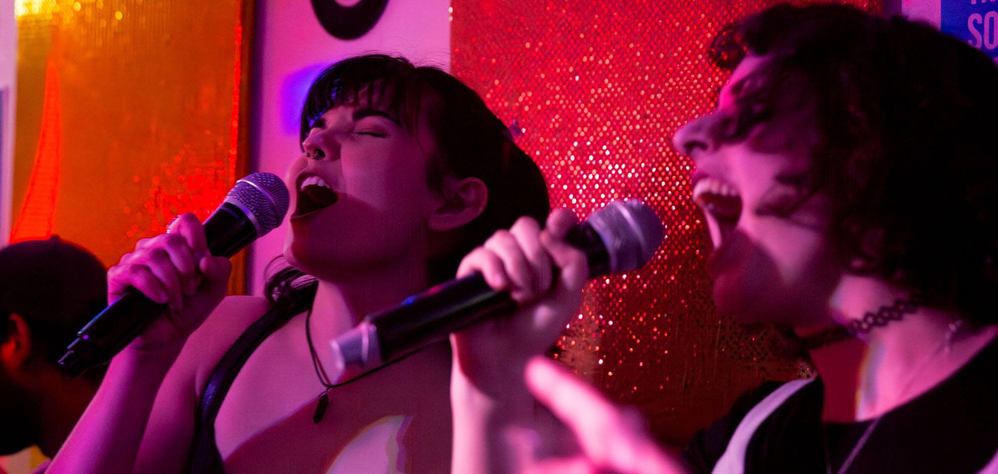 Friends singing together on stage at Benjys under pink lights